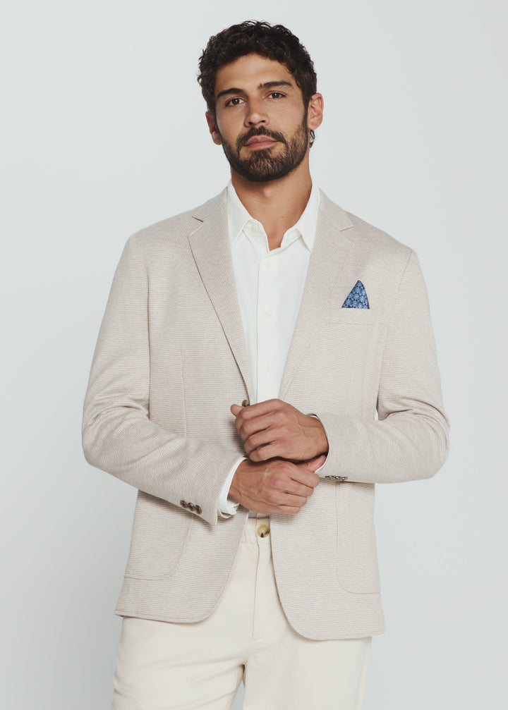Man wearing a beige suit with a white shirt and blue pocket square on a light gray background