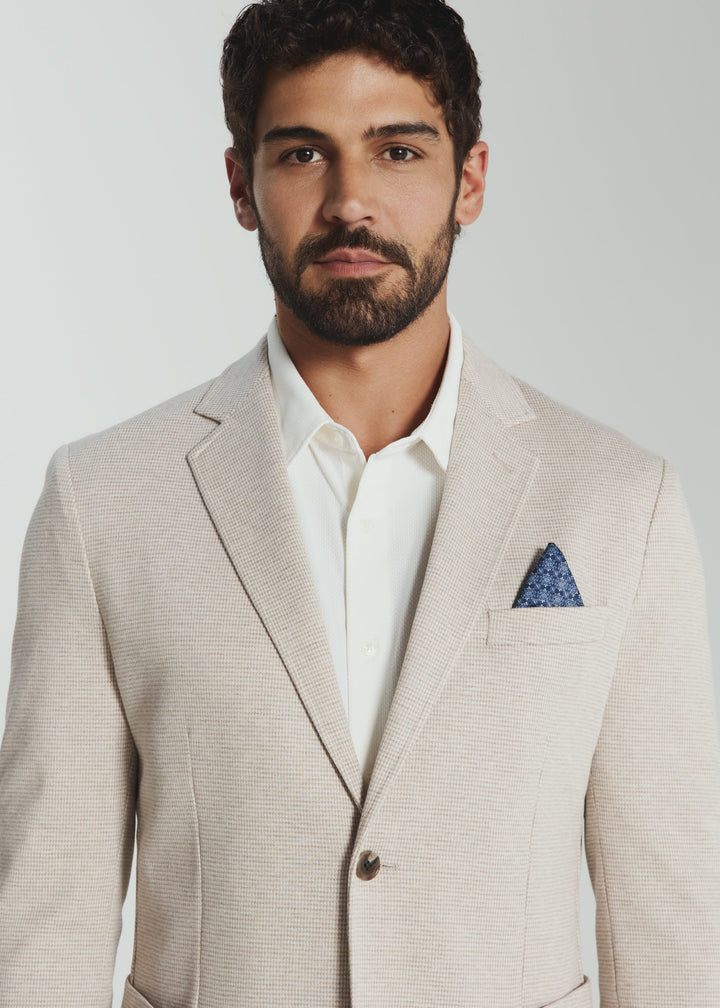Man wearing a beige suit with a white shirt and blue pocket square on a light gray background